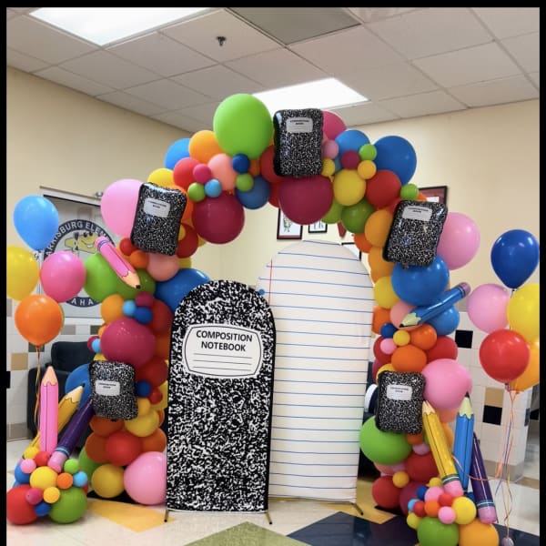 Colorful balloon arch with notebook cutouts and oversized pencils