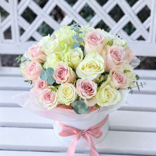 Bouquet of pale pink and cream roses in a white hatbox with a pink ribbon