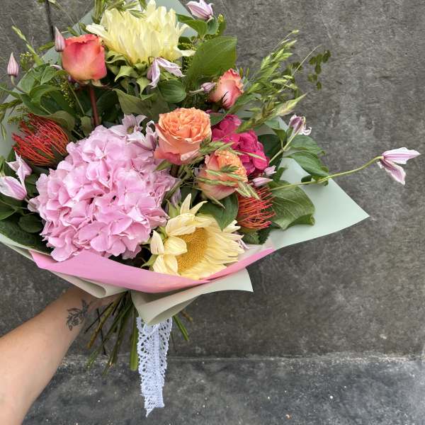Handheld bouquet of pink, peach, and cream flowers wrapped in pastel paper