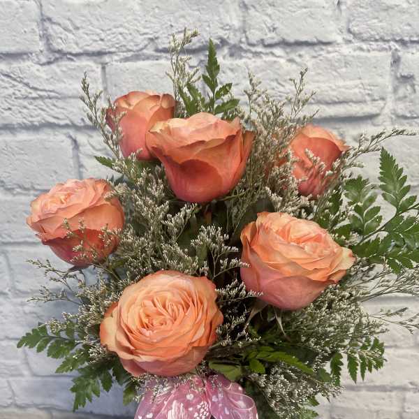 Peach roses in a glass vase with a pink ribbon