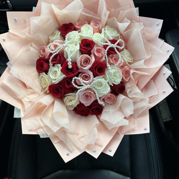 Bouquet of red, pink, and white roses wrapped in pale blush paper