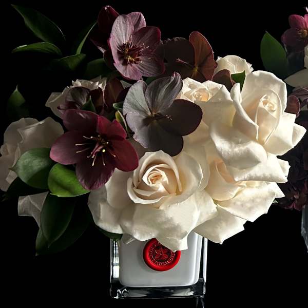 White roses and dark burgundy flowers arranged in a clear square vase