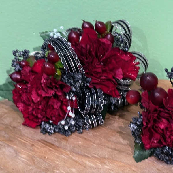 Two red floral arrangements with dark ribbon and berry accents on a table