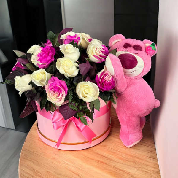 Pink and white roses in a round box beside a pink teddy bear
