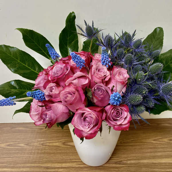 Pink roses and blue thistle in a white vase