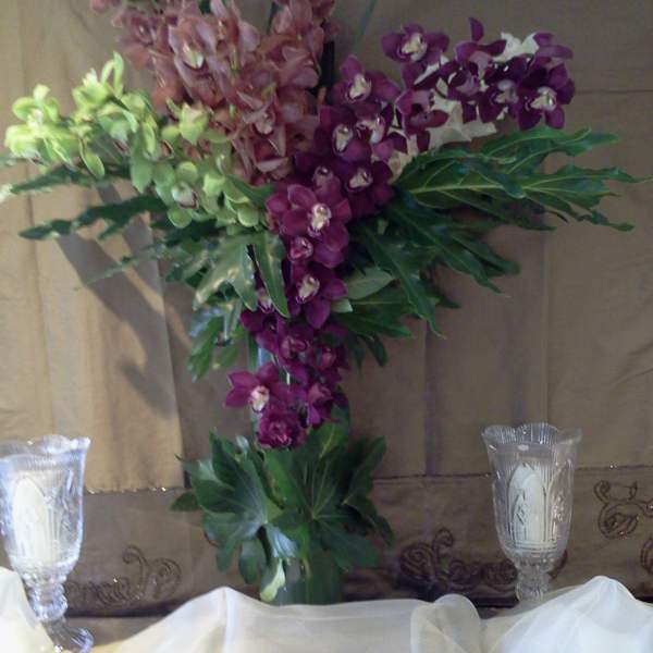 Tall orchid arrangement in purple and green with a glass vase