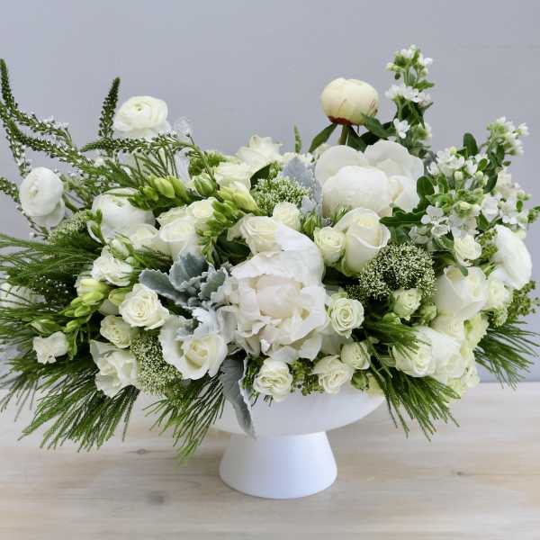 Low white pedestal arrangement with white roses, peonies, and other white blooms