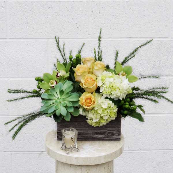 Arrangement of yellow roses, hydrangeas, orchids, and succulents in a rectangular container with a candle