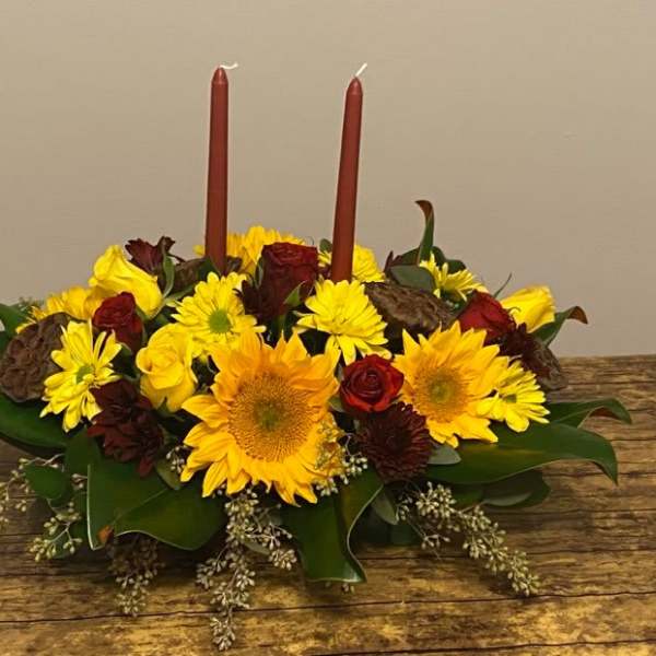 Low floral centerpiece with yellow sunflowers and red roses around two red candles