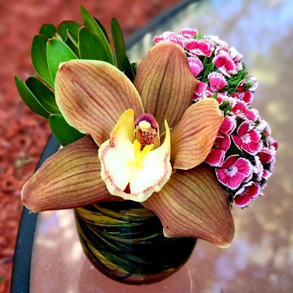 Orchid arrangement with pink mini carnations in a glass vase
