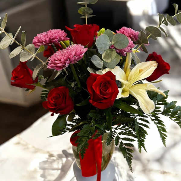 Bouquet of red roses, pink chrysanthemums, and a pale lily in a glass vase
