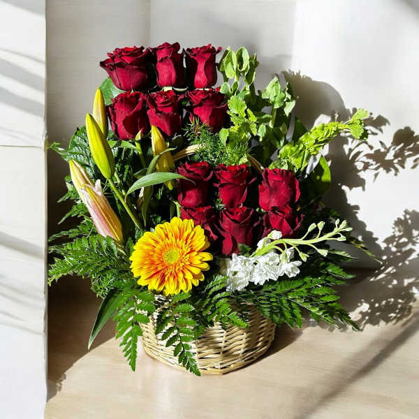 Basket arrangement of red roses, yellow lily buds, and a yellow gerbera daisy