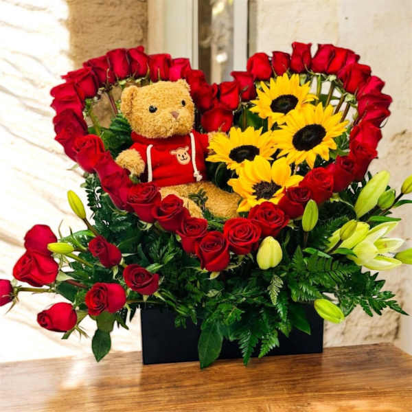 Heart-shaped rose arrangement with a teddy bear and sunflowers