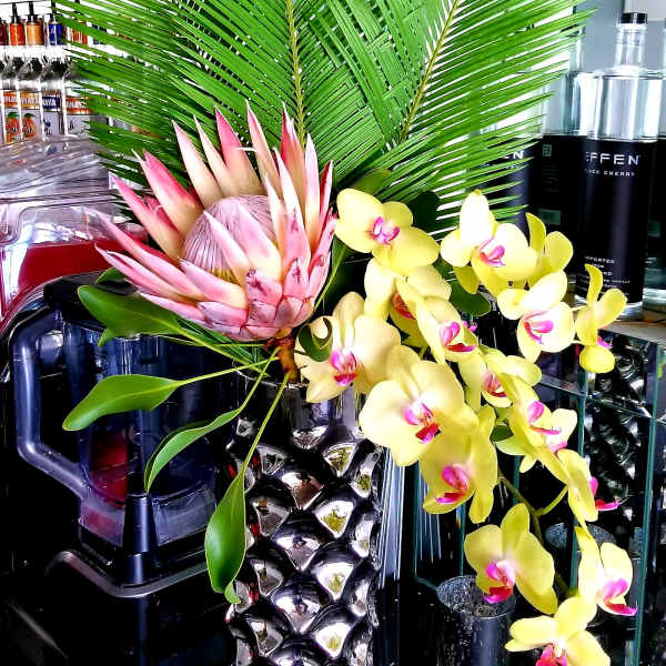 Tropical arrangement with pink protea and yellow orchids in a metallic pineapple vase
