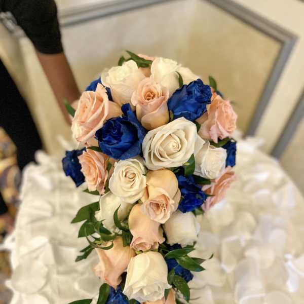 Bouquet of cream, blush, and blue roses with greenery