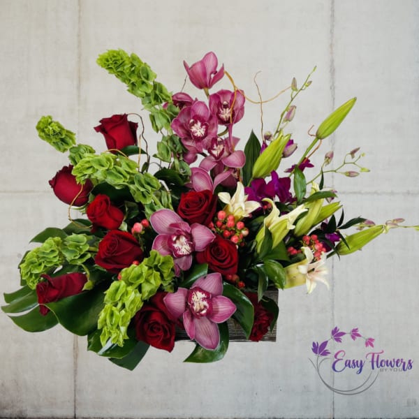 Arrangement of red roses, pink orchids, white lilies, and green blooms in a rectangular vase