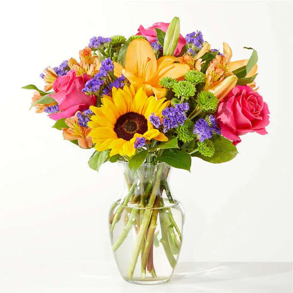 Mixed bouquet of sunflowers, roses, and lilies in a clear glass vase
