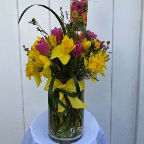 Yellow and pink tulips arranged in a clear glass vase with a yellow ribbon