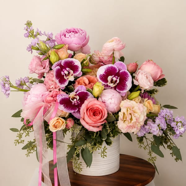 Pink and lavender floral arrangement in a white vase with ribbon