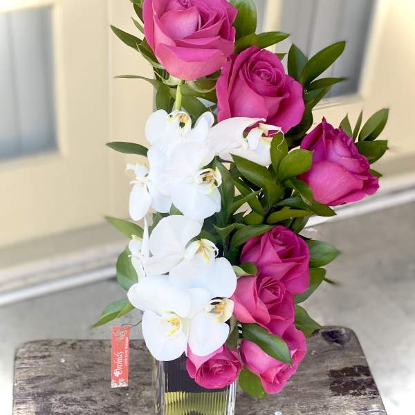 Pink roses and white orchids arranged in a clear glass vase.
