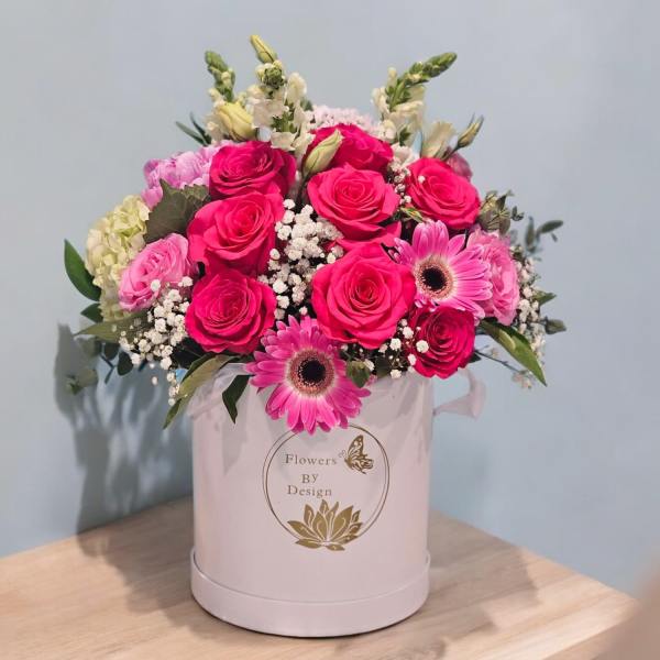 Pink roses and gerbera daisies arranged in a round hatbox