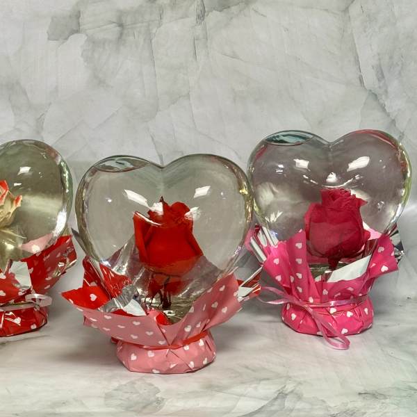 Three roses in heart-shaped glass holders with pink and red wrapping