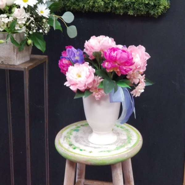 Pink and purple flowers arranged in a white vase on a stool