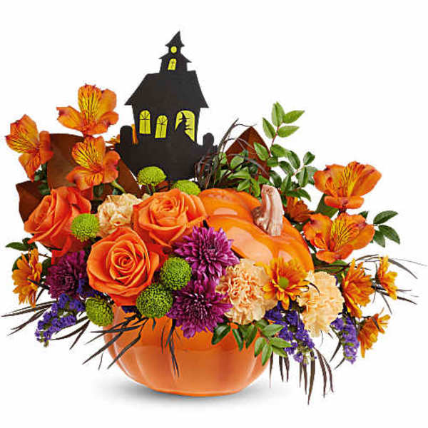 Orange floral arrangement in a pumpkin container with a haunted house pick