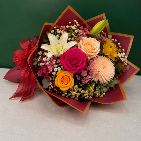 Mixed bouquet with roses, lilies, and a chrysanthemum wrapped in burgundy paper