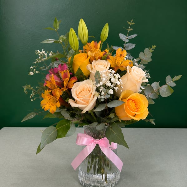 Bouquet of yellow and cream roses with orange flowers in a glass vase