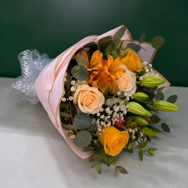 Bouquet of peach and yellow roses with orange lilies wrapped in pink paper