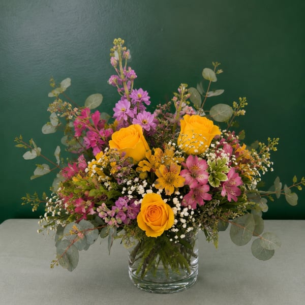 Mixed bouquet of yellow roses and pink flowers in a glass vase