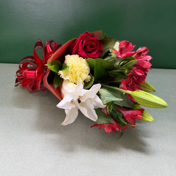 Bouquet of red roses, white lilies, and pink alstroemeria with a red ribbon