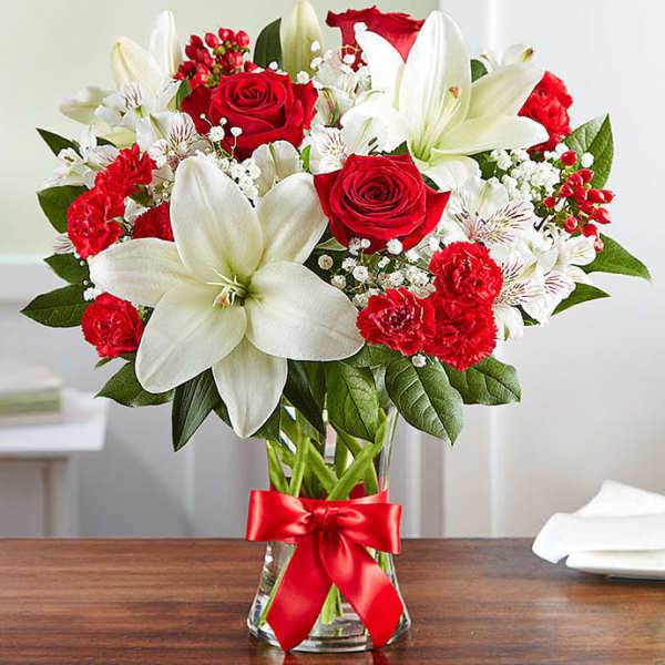 Red roses and white lilies in a clear glass vase with a red ribbon