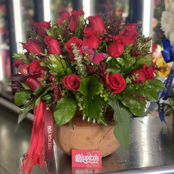 Red roses arranged in a round terracotta pot with a ribbon.