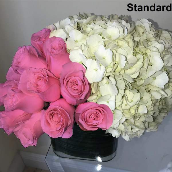 Low arrangement of pink roses and white hydrangeas in a square glass vase