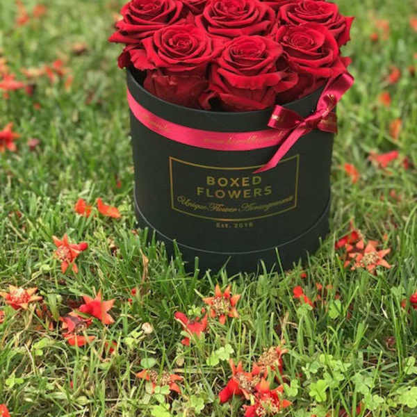 Red roses arranged in a black round box with a pink ribbon