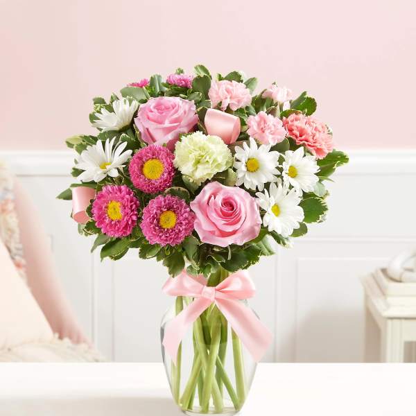Pink and white mixed bouquet in a clear glass vase with a pink ribbon
