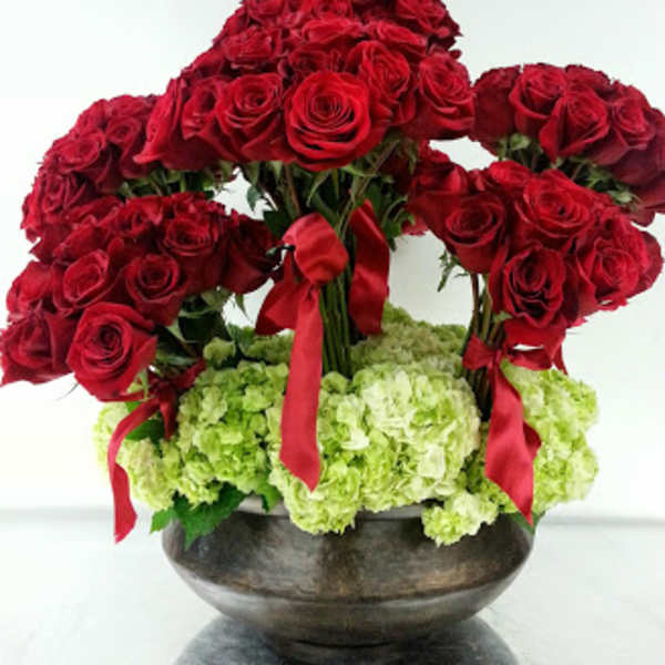 Red rose arrangement with green hydrangeas in a dark bowl vase