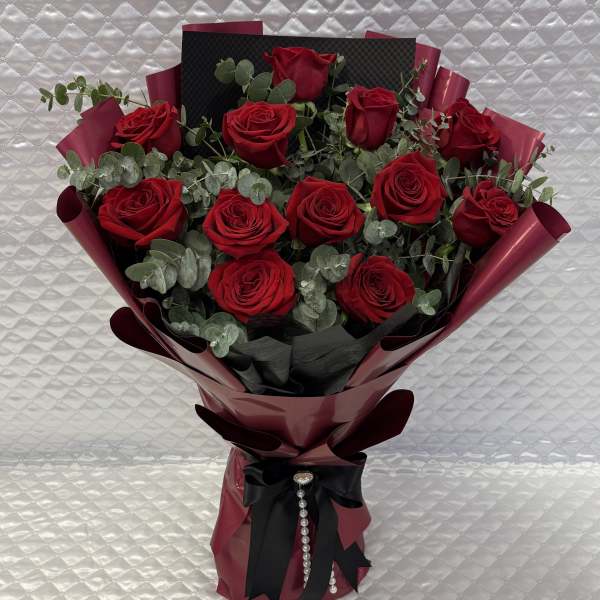 Bouquet of red roses wrapped in burgundy paper with a black ribbon