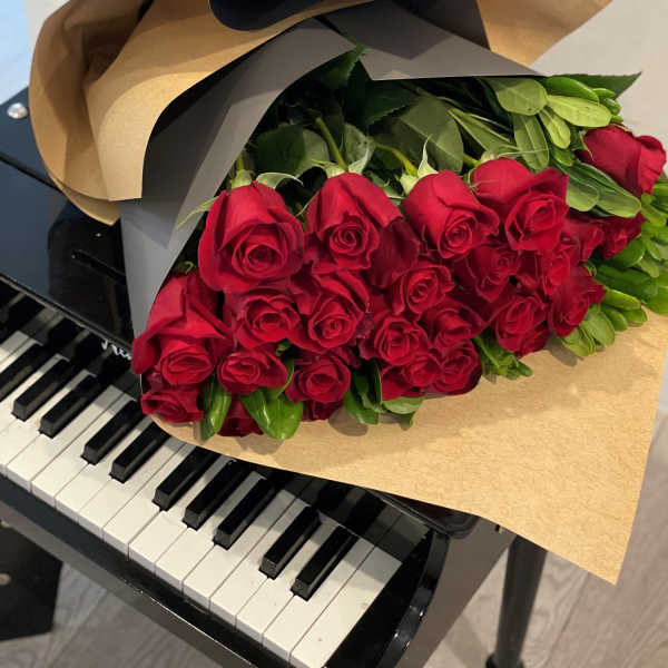 Bouquet of long-stem red roses wrapped in kraft paper resting on a black piano keyboard