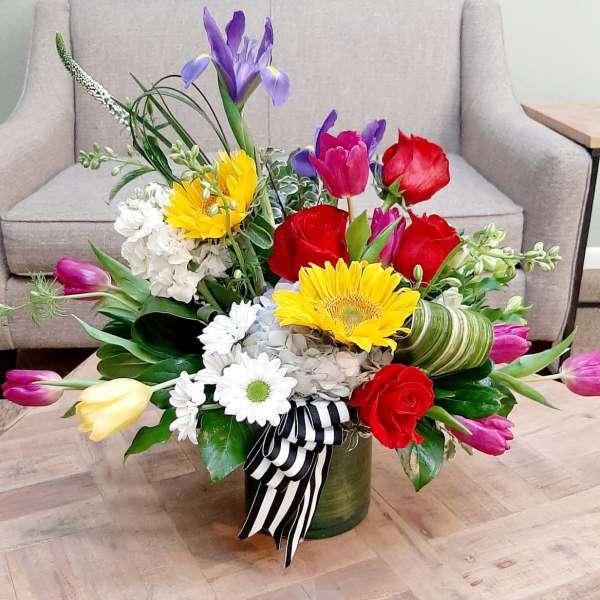 Colorful mixed flower arrangement in a green vase with a striped ribbon