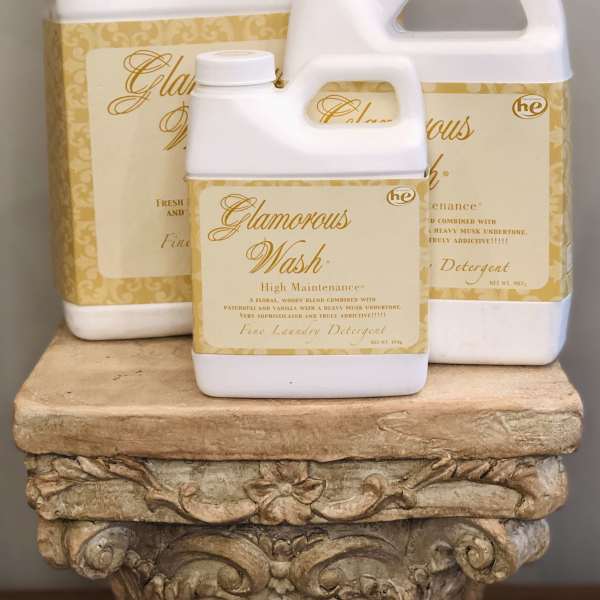 Three white laundry detergent jugs with gold labels stacked on a decorative pedestal.