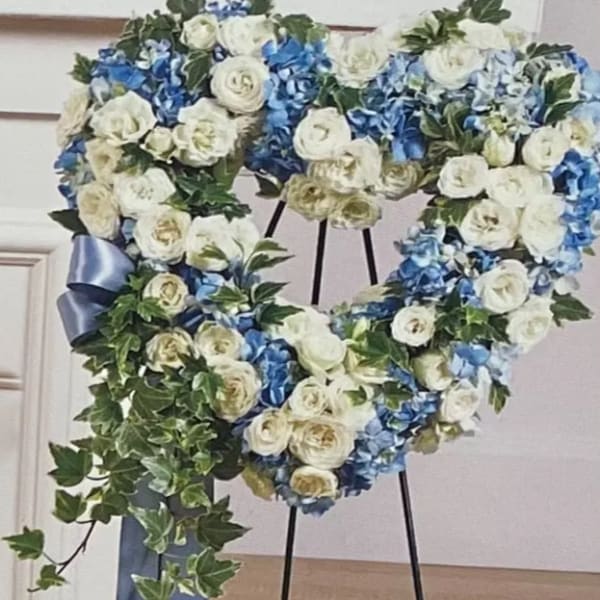 Heart-shaped floral wreath with white roses and blue hydrangeas on a stand