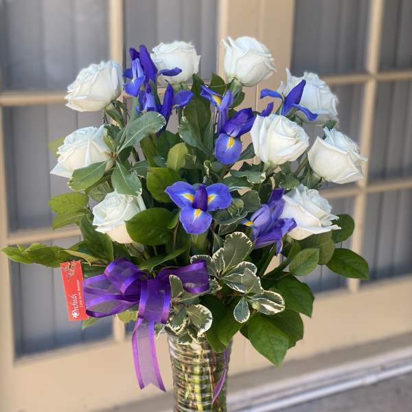 White roses and blue irises in a glass vase with a purple ribbon