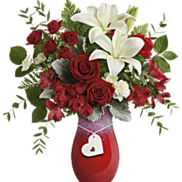 Red roses and white lilies in a red vase with a heart tag