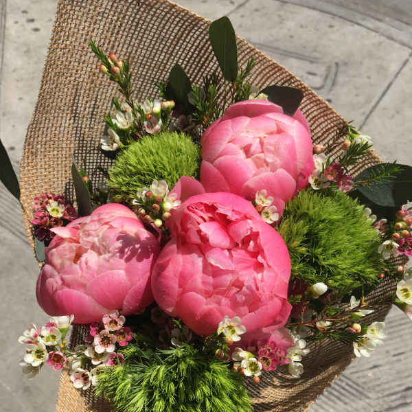 Pink peony bouquet with small white blossoms wrapped in burlap