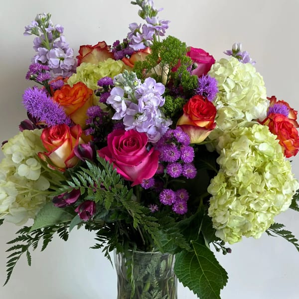 Mixed bouquet of roses, hydrangeas, and purple flowers in a glass vase