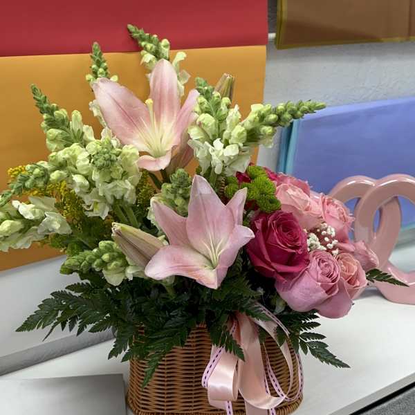 Pink lilies and roses arranged in a wicker basket with ribbon