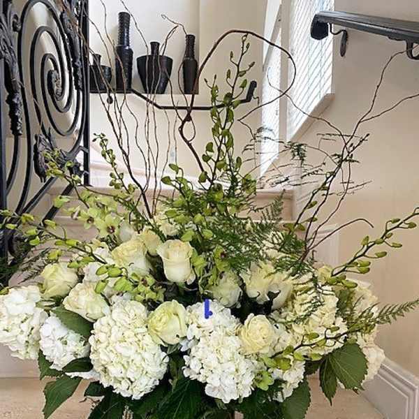 Large white hydrangeas and roses with green orchids in a tall glass cylinder vase